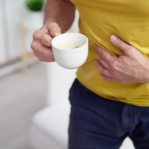 Męczy Cię zgaga po kawie? Odczuwasz pieczenie w żołądku? Sprawdź, dlaczego czasami po kawie boli brzuch. Mężczyzna w żółtej koszulce łapie się za brzuch po wypiciu filiżanki kawy.