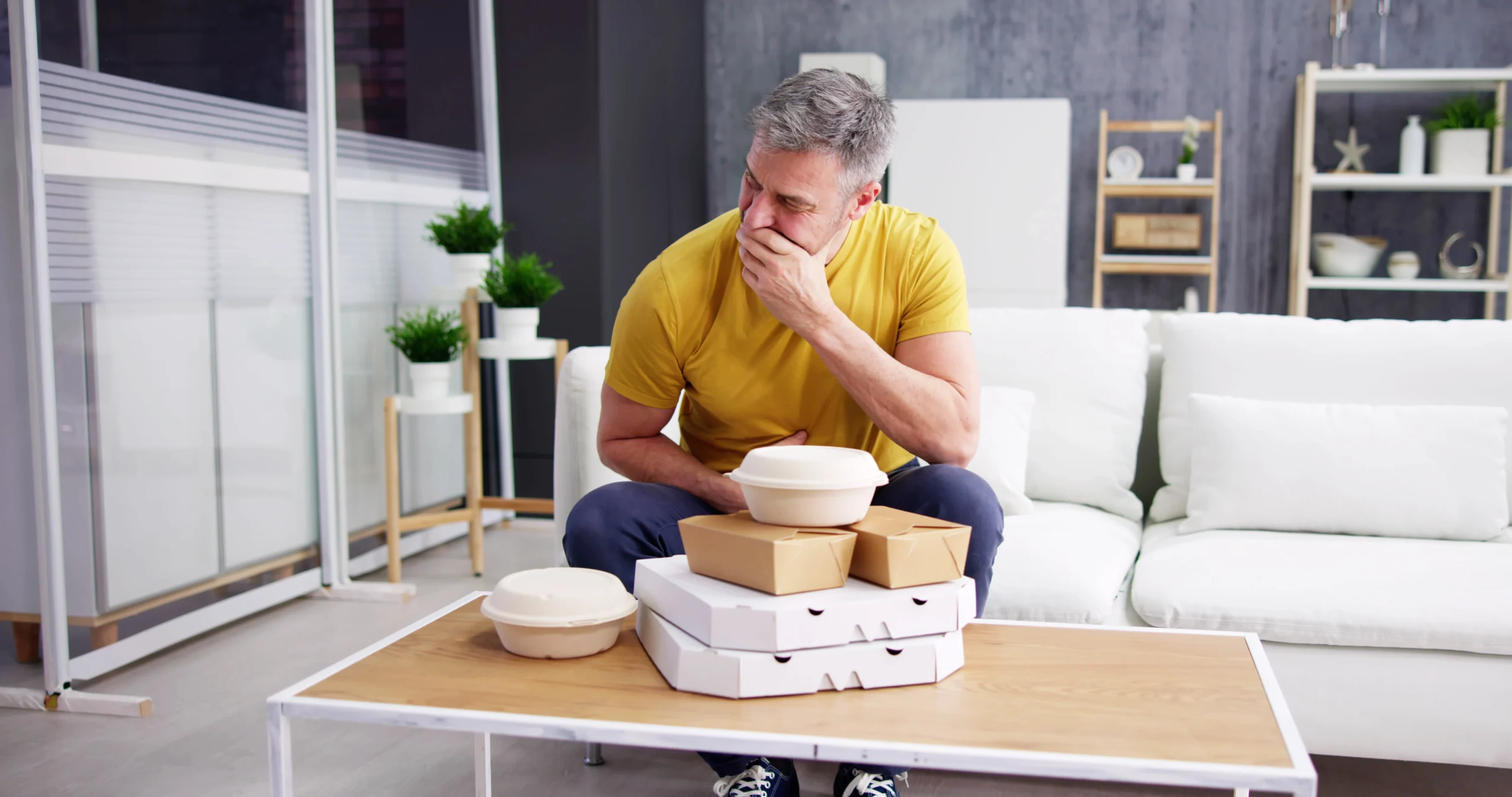 mężczyzna siedzi na kanapie przed zamówionym jedzeniem na wynos z grymasem świadczącym o zgadze